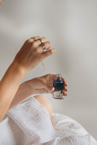 One hand applying a drop of liquid on the second hand, which is holding a brown glass jar